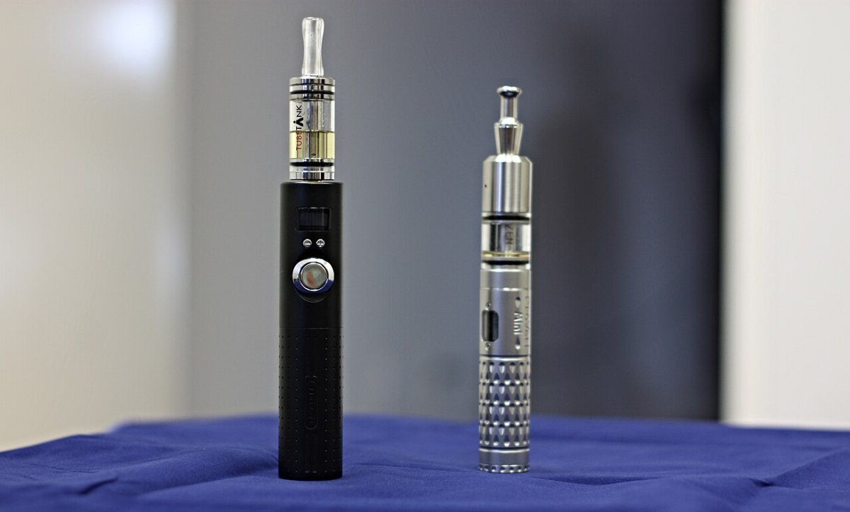 Două țigări electronice tip stilou, una mai simplă și una mai elaborată, pe o masă Două țigări electronice tip stilou, una mai simplă și una mai elaborată, pe o masă